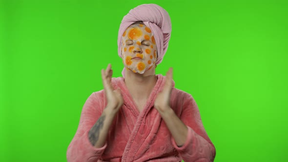 Young Man in Bathrobe with Face Mask Spraying Perfume on Neck