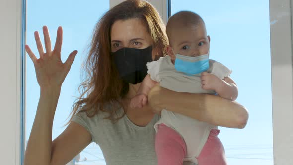 Mother in Medical Mask Communicated with Baby on Hands Through Glass Window