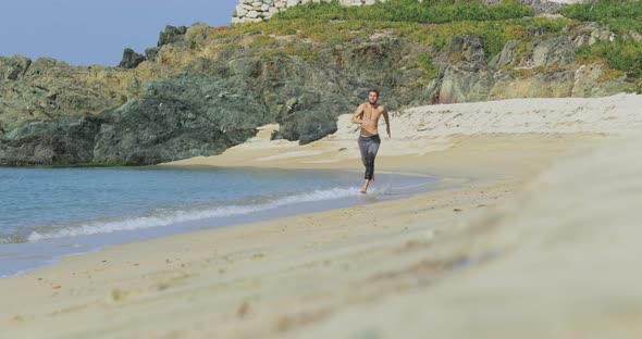 The Handsome Man with a Perfect Athletic Body in Gray Trousers Having Fun on a Deserted Beach in the