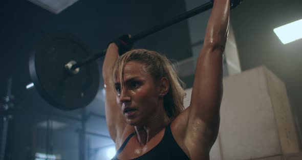 a Female Weightlifter Performs a Barbell Lift in a Dark Gym. a Woman Lifting a Heavy Bar Over Her