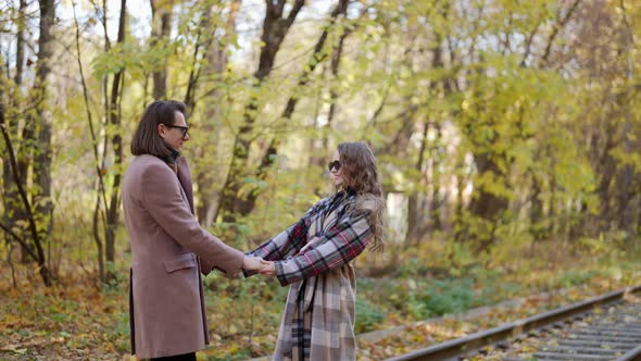 a Man and a Woman in a Coat and Dark Glasses Hold Hands and Stand on the Rails Against the