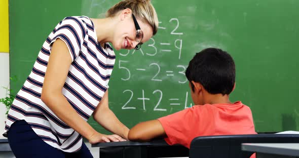 Teacher helping schoolboy with their studies in classroom