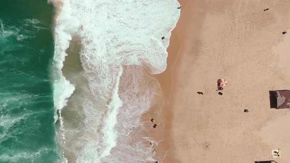 Static aerial drone showing endless wild sea waves breaking on the sandy coast line while people han