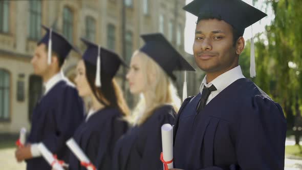 Mixed-race graduate student with diploma smiling into camera, exchange program
