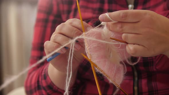 A Woman in Red Plaid Shirt Knits a Piece of Clothing From a Thin Pink Yarn