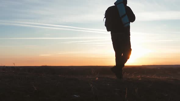 Silhouette of a Man with a Backpack Against Bright Sky Sunset. Sun Goes Down. Travel Concept. Slow