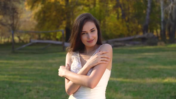 Portrait of Beautiful Brunette Bride with Long Hair Is Basking in Sunny Rays at Autumn Park