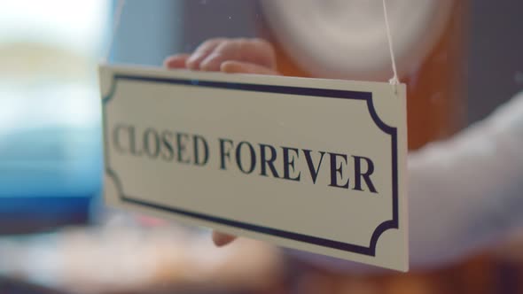 Close Up of Human Hand Hanging Closed Forever Sign on Glass Door of Cafe or Store