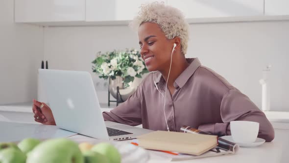 Cheerful African American Woman Laughing Sits at Kitchen Table with Laptop