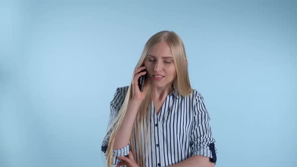 Pleasant-looking Young Lady Speaking with Somebody By Smartphone on Blue Background.