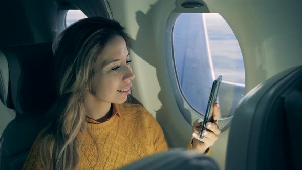 Smiling Lady Is Browsing Her Phone During the Plane Flight