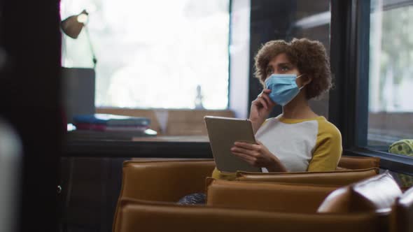 African american woman wearing face mask using digital tablet at modern office