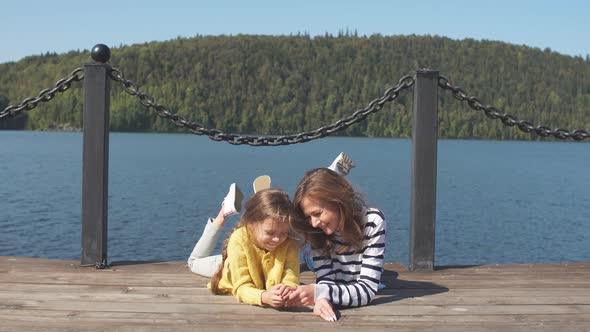 Mother and Daughter Sitting on Pier Warm Autumn Day