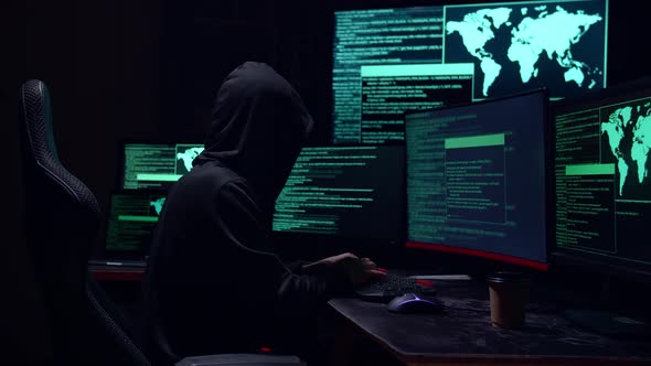 Male Hacker Hacking With Multiple Computer Screens In Dark Room