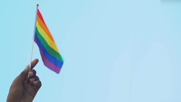 Hand of African-American male holding rainbow flag against sky