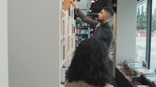Male Student Reaching for Book in Library