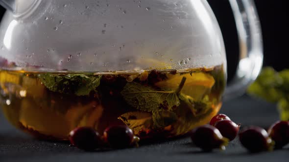 Close Up of a Teapot with Lemon, Tea and Herbs in the Water, Rosehip Near It, 