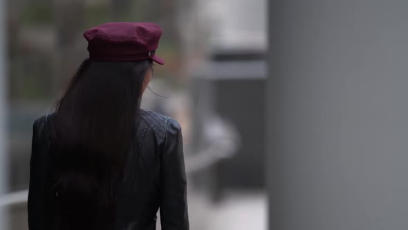 a Beautiful Dark-haired Female Model in a Purple Cap and Leather Jacket Poses in a Public Place Near