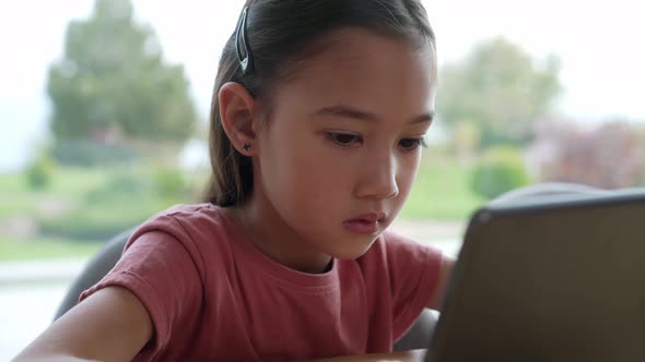 Serious Asian girl typing on tablet