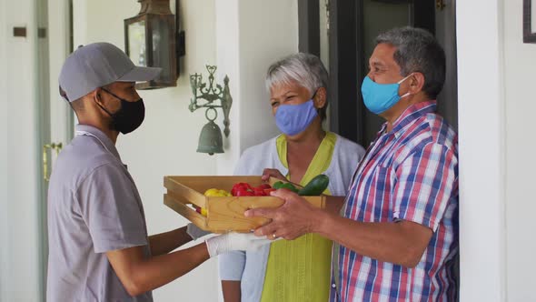 Senior mixed race couple and food delivery man at door wearing face masks