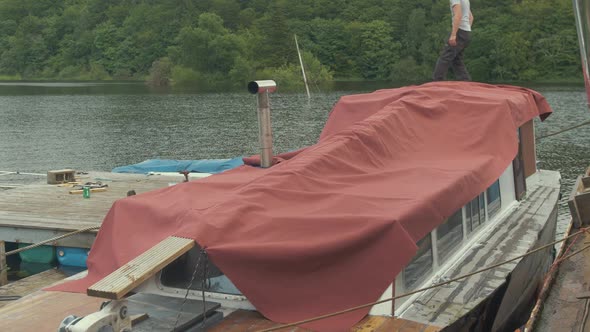 Young man securing waterproof canvas cover over wooden boat