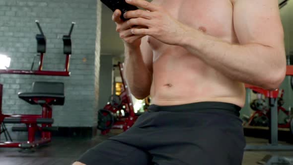 Focused Shot of Man Toned Abs As He's Using His Phone in Between Gym Exercises