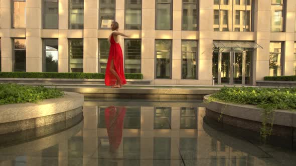 Beautiful Young Girl Dancing on the Street of a Modern City and Is Reflected in the Water