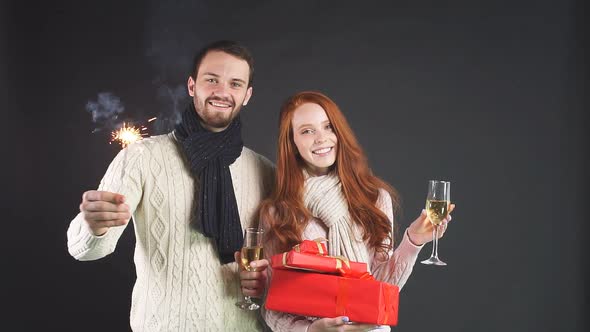 Young Happy Couple Standing in Studio with Sparklers and Gifts, Smiling Looking at Camera.