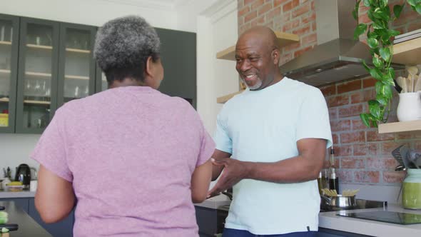 Happy african american senior couple dancing together in kitchen
