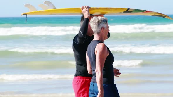 Senior couple carrying surfboard over head while walking on beach