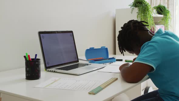 African american boy doing homework looking at laptop with copy space at home