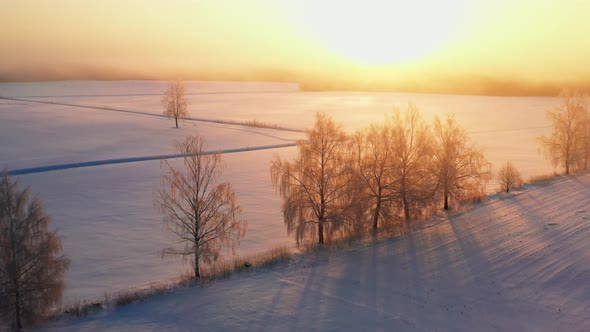 Aerial passage over white countryside fields during a foggy winter sunrise