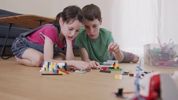 Girl and a boy playing and constructing with toy bricks on the living room floor