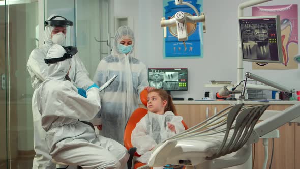 Pediatric Dentist and Nurse in Ppe Suit Interrogating Kid Patient