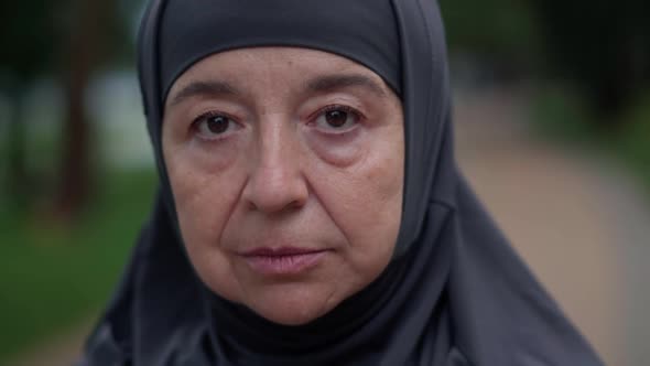 Closeup Face Sad Senior Muslim Woman in Hijab Looking at Camera with Brown Eyes Standing Outdoors