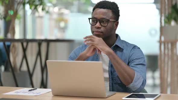 Young African Man Thinking While Using Laptop in Modern Office