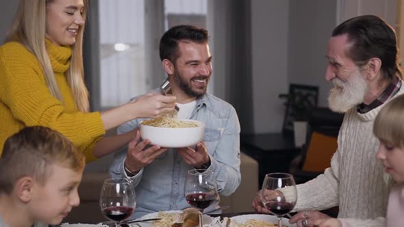 Happy Cheerful Mother Putting Spaghetti on Grandfather's Plate During Family Dinner