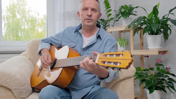 Senior Man Plays Acoustic Guitar and Sings in Apartment Living Room