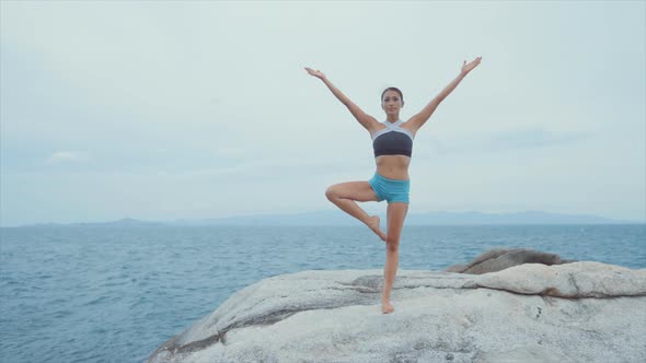 Woman Standing on One Leg and Meditating on Rocks Near Ocean