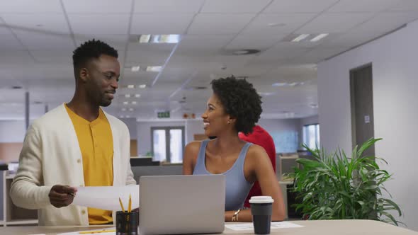 Happy african american male and female business colleagues talking and using laptop