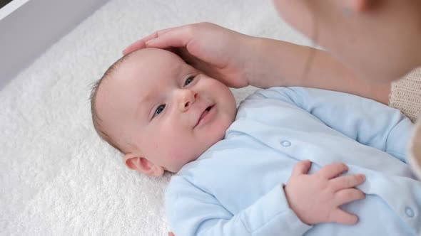 Adorable Baby Boy Smiling at Mother While She is Stroking Him on Dressing Table