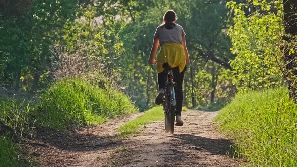 Woman on Bicycle Rides Along Green Forest Path on Sunny Summer Day Slow Motion