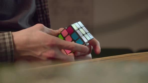 Man Solves Rubik Cube Sitting at Table in Office Closeup