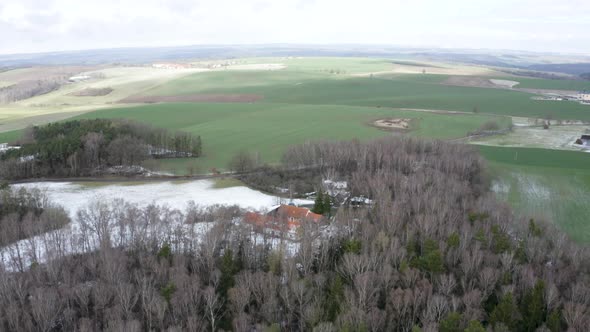 Secluded farm ranch in leafless tree grove and snowy field, Czechia.