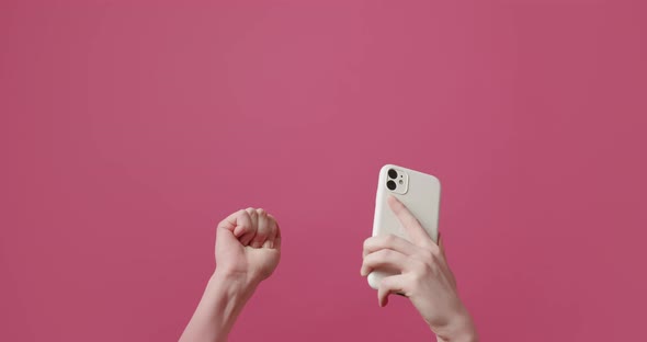 The Young Woman Uses a SmartPhone and Shows the Like Symbol on Pink Background