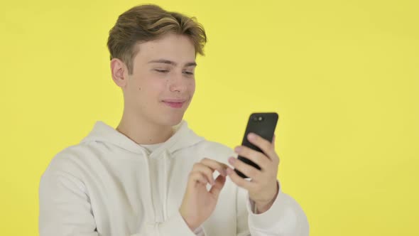 Young Man Browsing Smartphone on Yellow Background