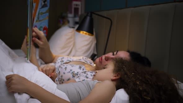 Child Care at Home Mom Takes Care of the Youngest Daughter Reads a Bedtime Story to the Children