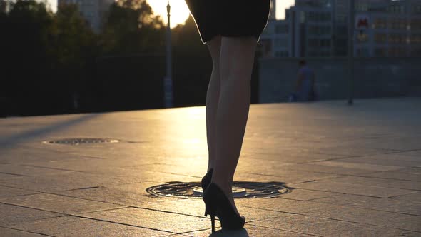 Follow To Female Legs in High Heels Shoes Walking Along City Street in Sunset Time