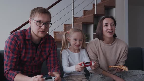 Woman, Man and They Child Playing in Video Games and Eating Pizza