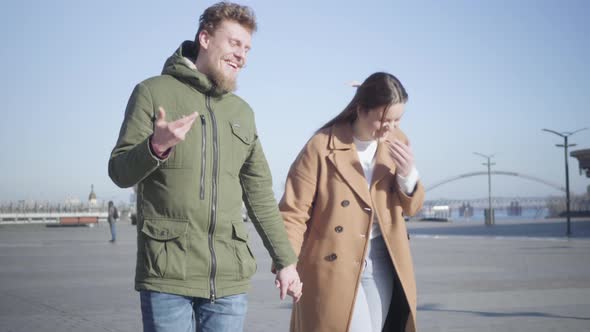 Portrait of Young Smiling Caucasian Man and Woman Talking As Walking Outdoors. Happy Couple Dating